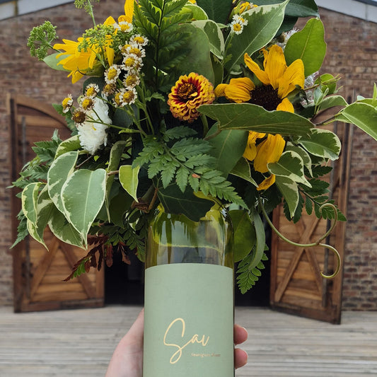 Bouquet of flowers in a green bottle held by a person against a brick wall.
